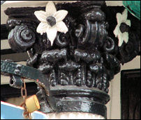 flower & scroll decoration on top of a cast iron column between two shops 